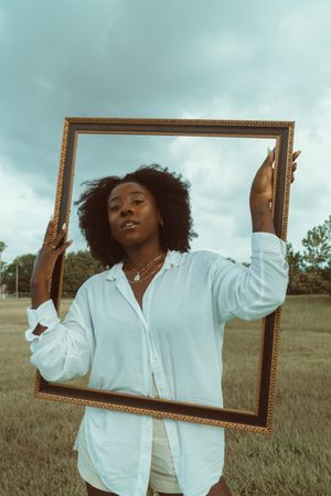 Portrait of Black woman in light shirt holding brown wooden frame