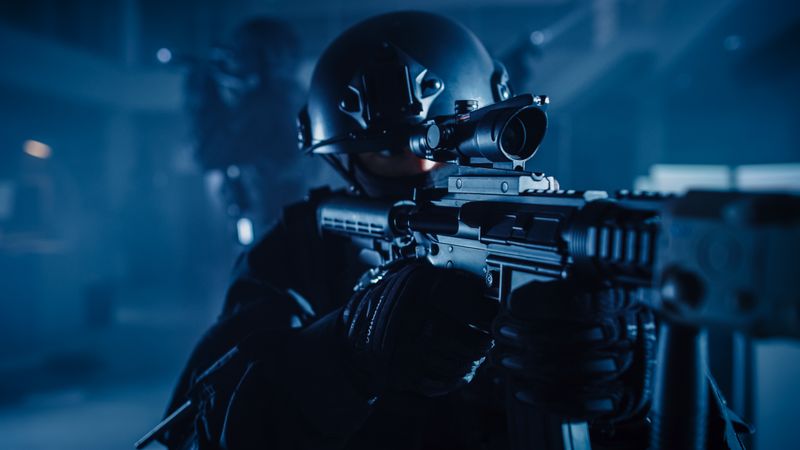 Close Up Portrait of Masked Squad Member of Armed SWAT Police Officers Who Storm a Dark Seized Office Building with Desks and Computers