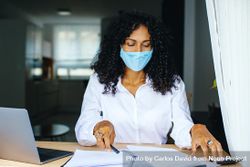 Woman in facemask holding a pen and working on documents 4N7kmb