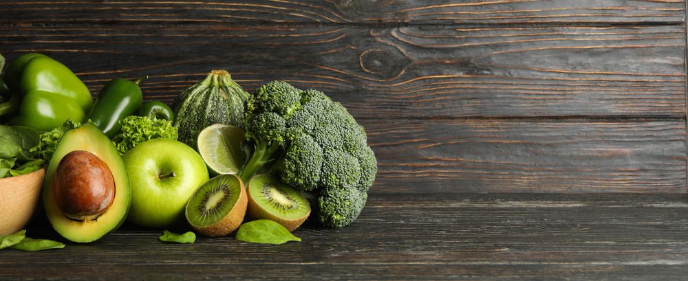 Green vegetables and fruits on wooden background