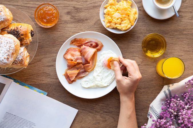 Person reading while eating bacon and eggs at table