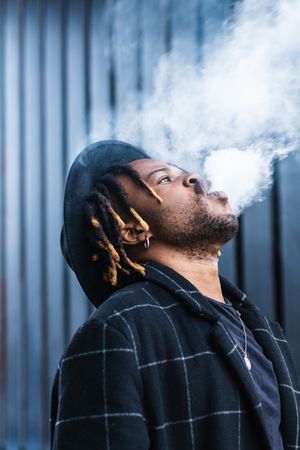 Black man exhaling cloud of smoke on street