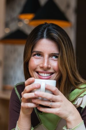 Contemplative cheerful woman with cup of coffee in cafe