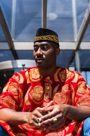 Thoughtful Black man in traditional clothes and headdress near building