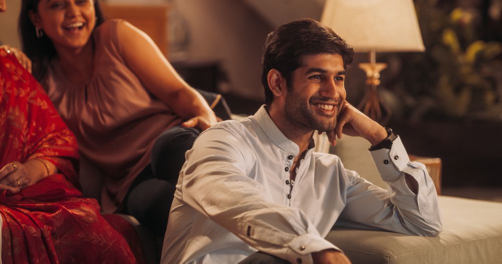 Portrait of Happy Indian Young Man Enjoying Movie Playing on TV at Home Together with his Family.
