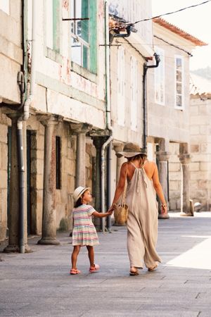 Mother and daughter walking in street along ancient building