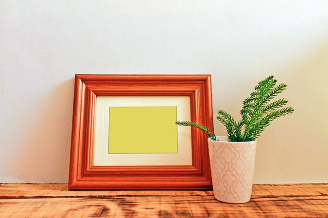 Wooden picture frame leaning against wall with branch in vase mockup