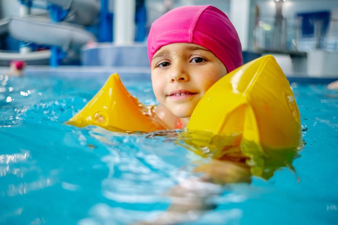 Cheerful girl in hat smiling and swimming in pool in water park