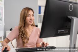 Confident Asian woman sitting in office and typing on keyboard while looking at monitor 5ag88b