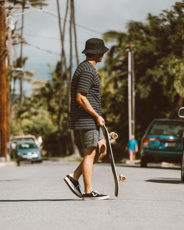 Side view of man holding skateboard walking down the street
