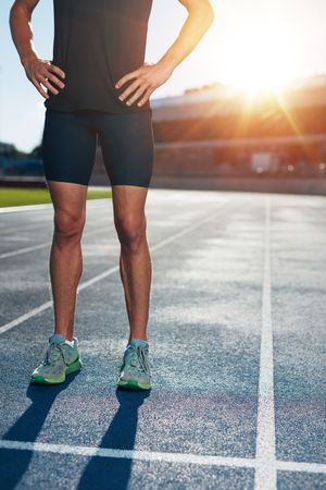 Shot of athlete’s body standing on race track with his hands on hips