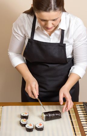 Female chef in apron cutting sushi rolls on table, vertical