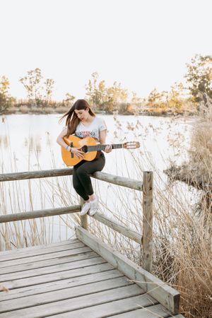 Young woman playing guitar near water