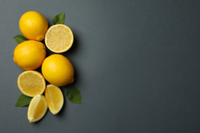 Fresh lemons with leaves on dark background, top view. Ripe fruit