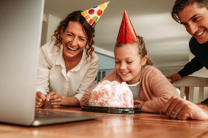 Family wearing party hats with birthday cake on table and looking at laptop