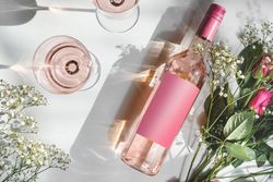 Rose wine bottle with empty pink mock up label, two wine glasses and romantic flower bouquet