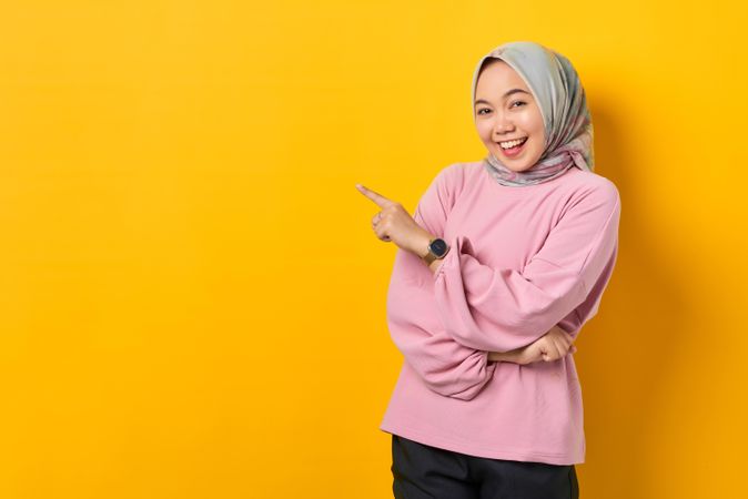 Smiling Muslim woman in scarf pointing up to her side