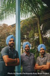 Three Indian men in blue turbans and gray shirts posing under palm tree in Dera Baba Nanka, India 0PjDO4