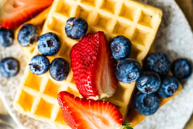 Close up of waffle breakfast with blueberries & strawberries served with syrup on the side