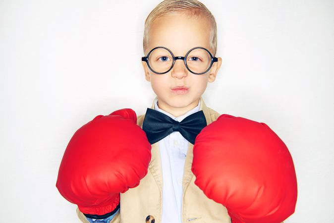 Serious blond boy wearing round glasses and red boxing gloves with a suit