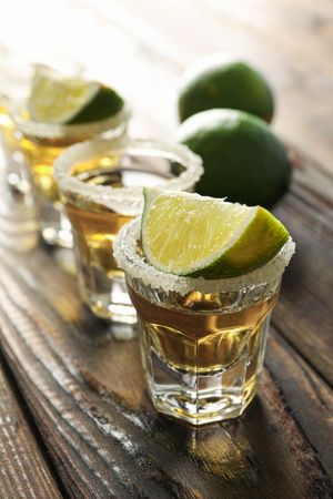 Tequila shots with salt and lime slices on wood table, closeup
