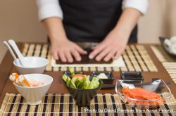 Hands of female chef ready to prepare sushi rolls, with fresh ingredients in the foreground 5n8q2b