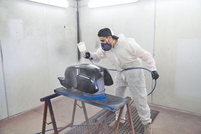 Man in dust suit painting motorbike tank in garage