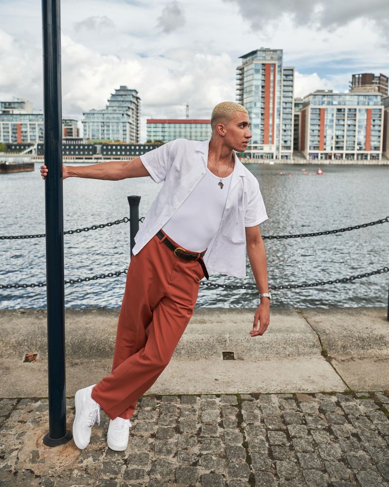 Stylish young man hanging onto a streetlamp on the waterfront