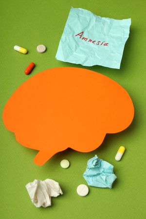 Orange paper cut out of brain on green background with pills and post it notes, vertical