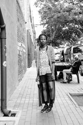 Young man poses on the sidewalk in fashionable clothing in shorts and a long coat