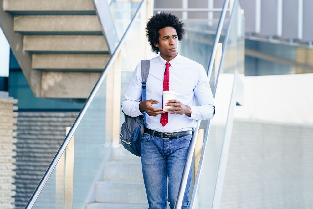 Calm man holding coffee walking down stairs