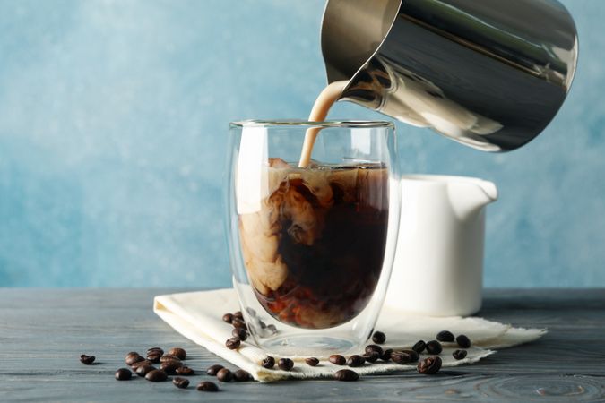 Milk is poured into a glass of coffee. Composition with ice coffee