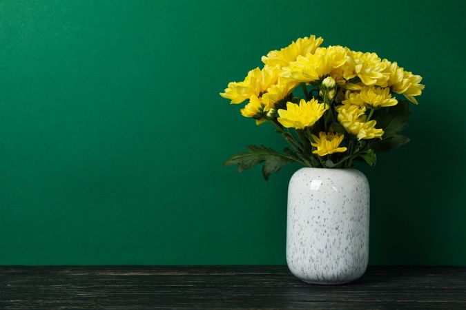 Vase with yellow chrysanthemums on wooden table, space for text
