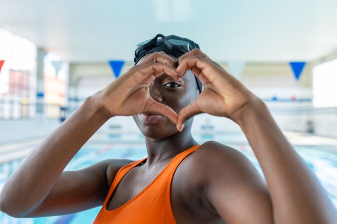 Black young woman making a heart shape with her hands at the swimming pool