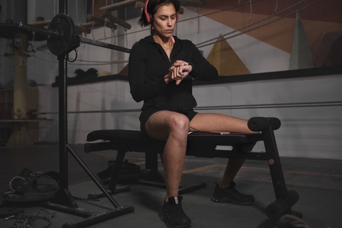 Athletic woman looking at watch on bench at gym