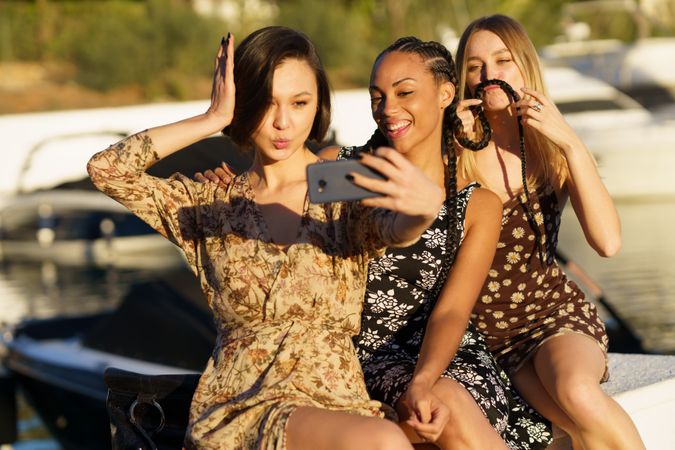 Three women sitting on wharf taking a silly selfie