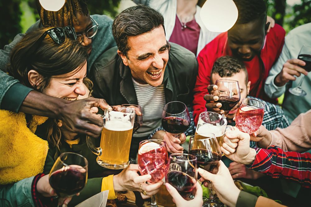 Group with many people celebrating a birthday toasting together with beers, wine and cocktails