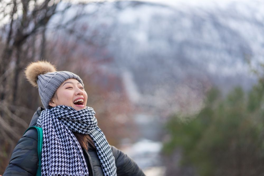 Pleased Asian female tourist in warm clothing at snowy nature