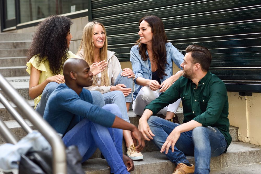 Happy friends sitting and chatting on outdoor cement staircase
