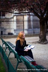 Woman sitting on green bench reading book in the park 0vrwx0