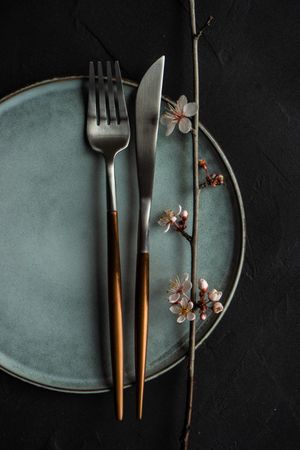 Top view of spring table setting with blooming tree branch on grey plate with silverware