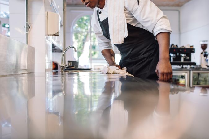 Cropped shot of waiter wiping the counter top in the kitchen with cloth