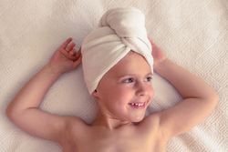 Smiling kid with towel on head on bed