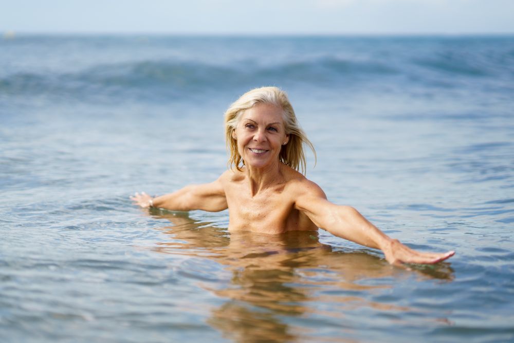Smiling mature woman in bathing in the sea with open arms