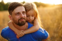 Man dressed in blue carrying daughter on his back in sunny meadow