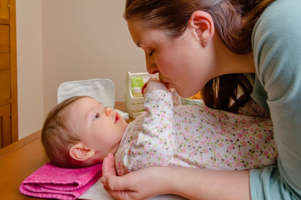 Mother kissing hands of her baby lying after changing diaper