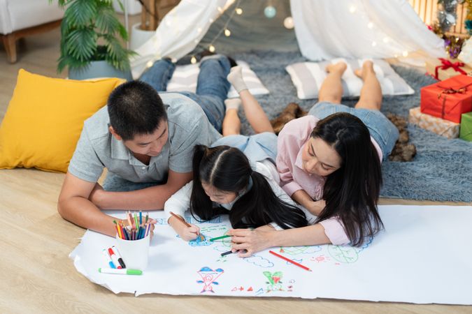 Happy Asian family drawing on paper together in the living room