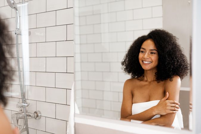 Black woman smiling at herself in the mirror next to a shower