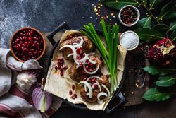 Top view of Georgian plate of abkhazura meat cutlets with pomegranate seeds, bay leaves & onions