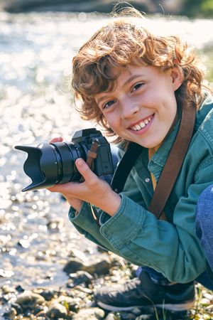 Cheerful boy with photo camera on shore near lake